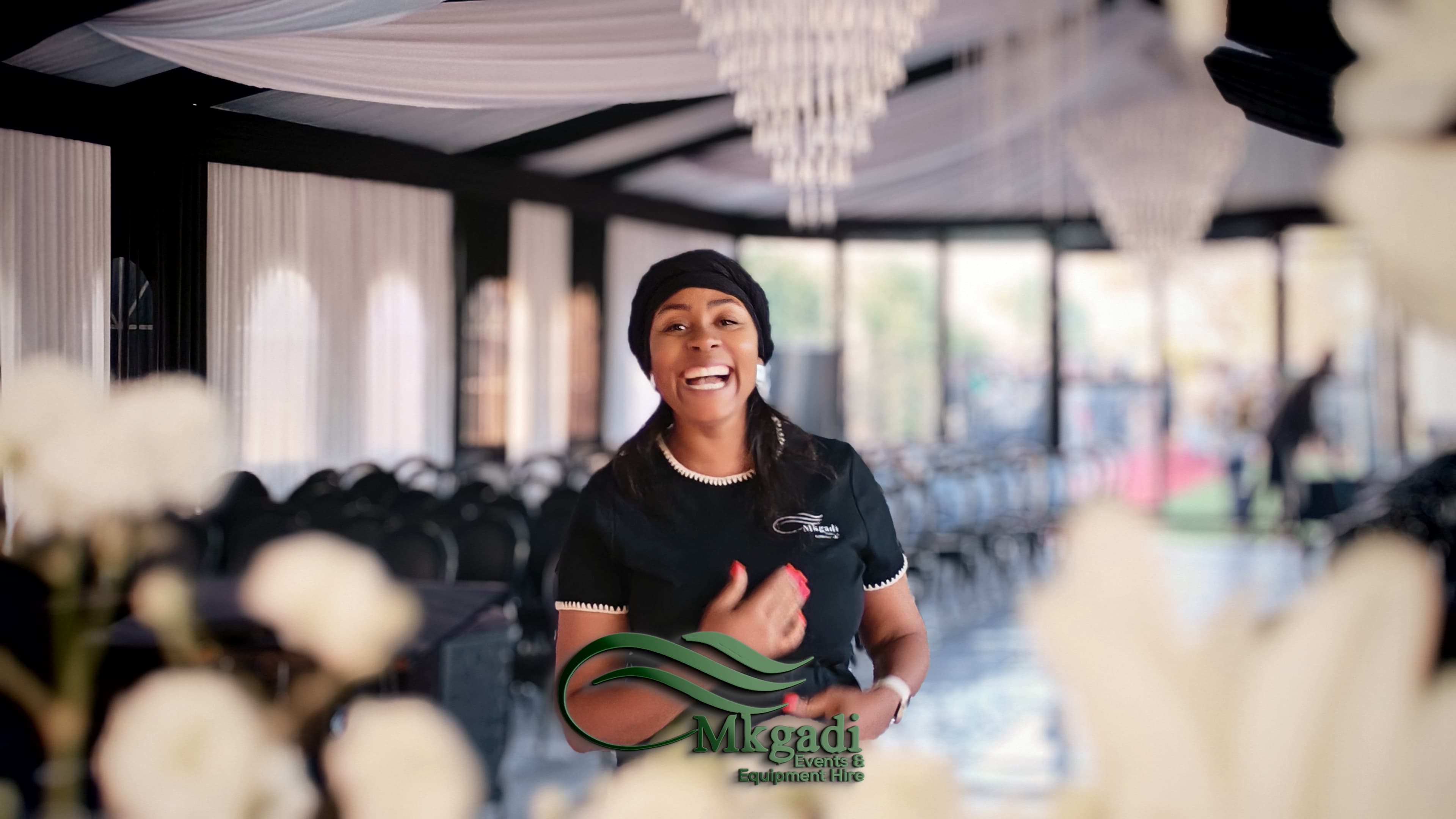 Richly decorated indoor event venue with green and white draping, round tables with floral centrepieces and warm ambient lighting
